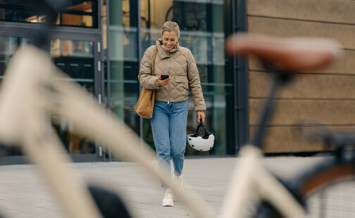 Lächelnde Frau hält Handy in der Hand und läuft auf ihr eBike zu.