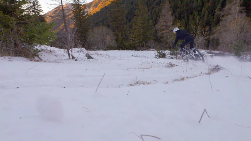 Un conducteur de VAE roule dans la neige, avec des arbres et un paysage hivernal en arrière-plan.