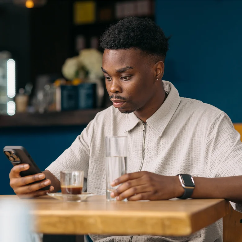 Man sitting in a restaurant and looking at his smartphone. There is water and coffee on the table.