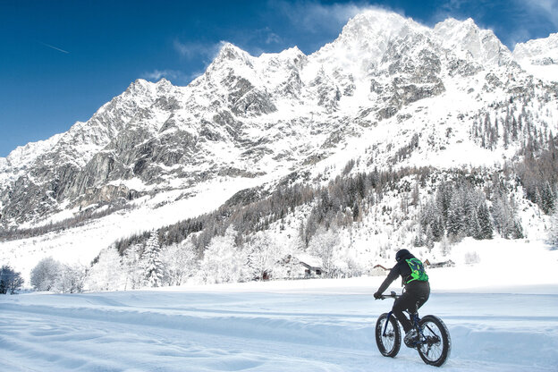 Un eBike attraversa un paesaggio innevato lungo, sullo sfondo si possono vedere montagne e foreste.