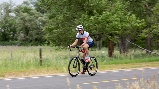 An eBike rider is riding along a country road, with a meadow and trees beside him.