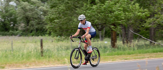 An eBike rider is riding along a country road, with a meadow and trees beside him.