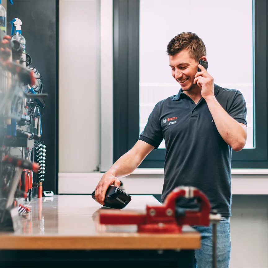 Ein Bosch-Mitarbeiter telefoniert mit einem Lächeln im Gesicht, während er auf ein Bosch-Produkt schaut, das auf einem Werktisch liegt.