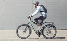 eBike rider drives on a paved pathlong, with a gray wall in the background.