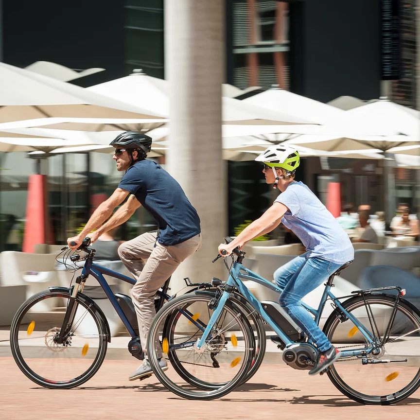 Ein Mann und eine Frau fahren auf ihren eBikes an einem Restaurant vorbei.