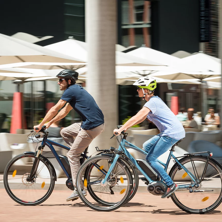 Un homme et une femme roulent sur leurs vélos électriques en passant devant un restaurant.