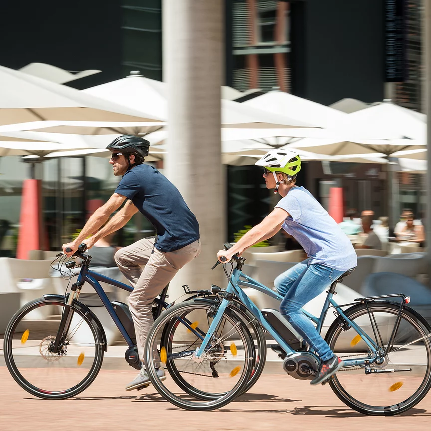 Ein Mann und eine Frau fahren auf ihren eBikes an einem Restaurant vorbei.