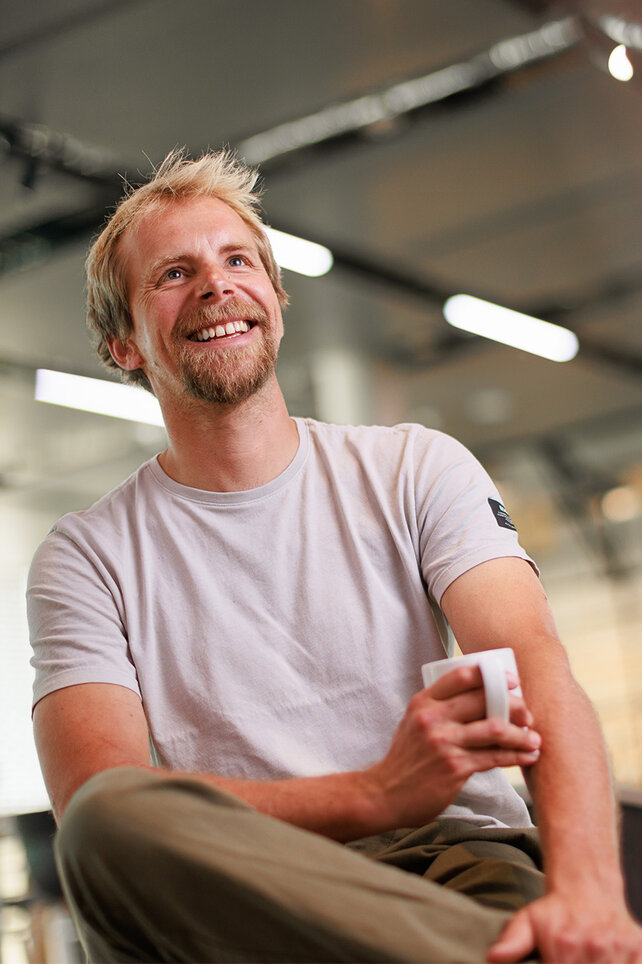 Photo of Harald Philipp, smiling with a coffee cup in hand while sitting in an office.