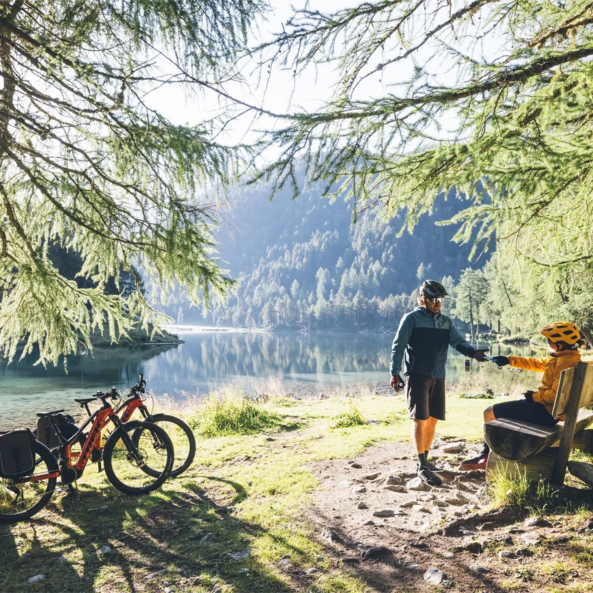 Deux cyclistes VAE font une pause au bord d’un lac entouré de forêt.