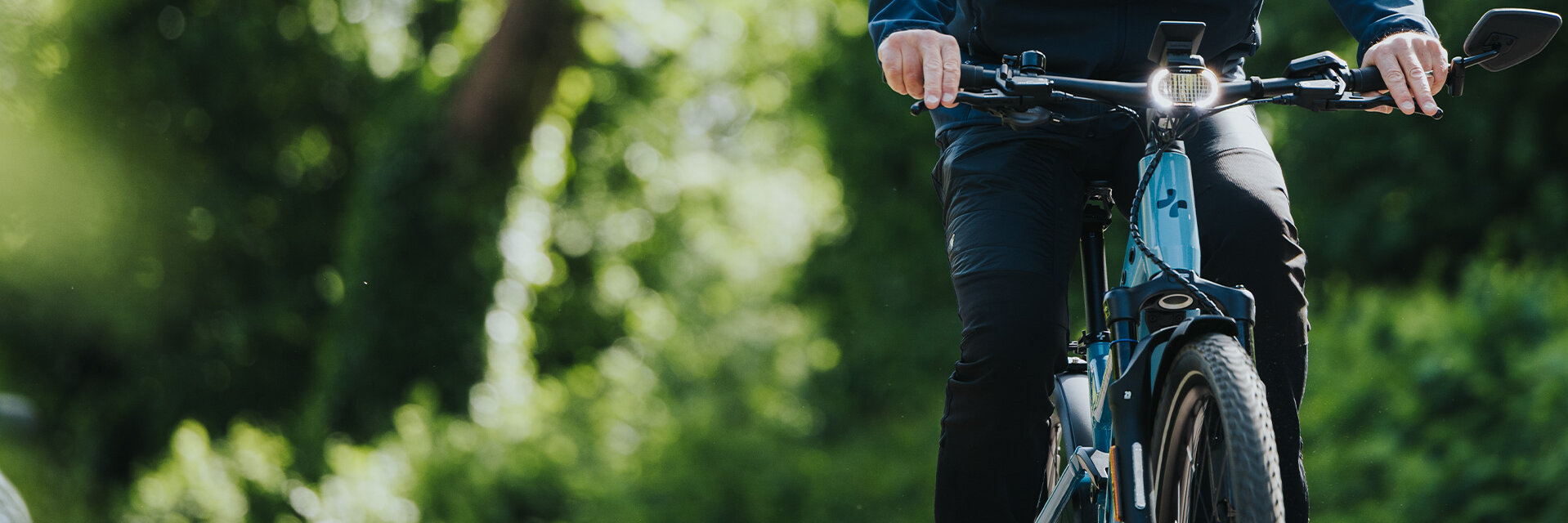 A man is riding his eBike along a road through a lush green forest.