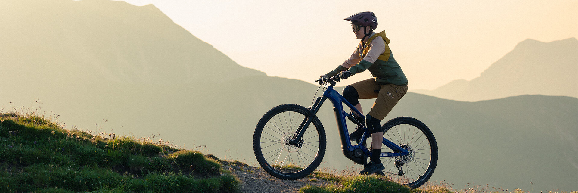 eBiker fährt mit einem eBike einen Hügel in der Natur hinauf. Im Hintergrund sind Berge zu sehen.