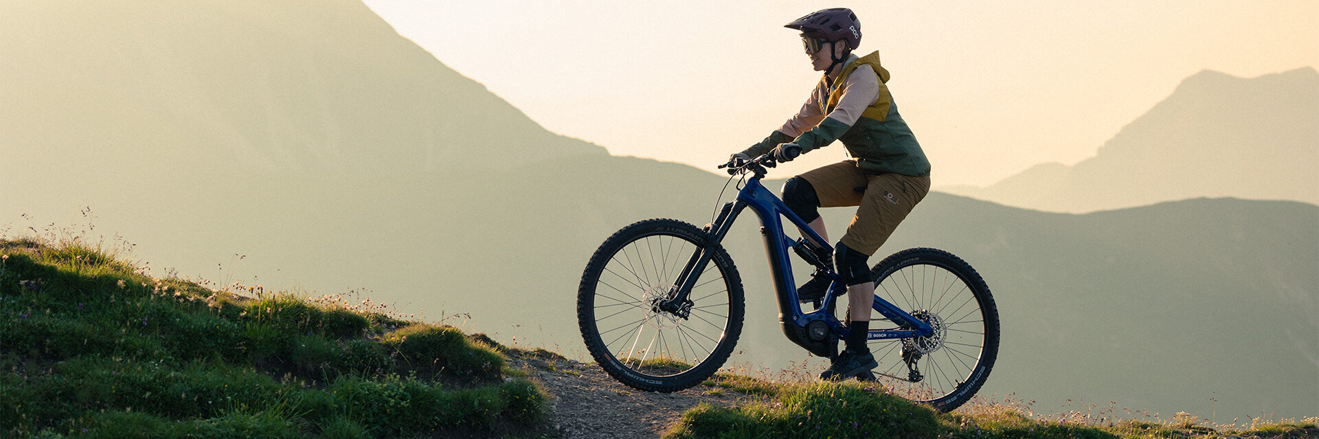 eBiker fährt mit einem eBike einen Hügel in der Natur hinauf. Im Hintergrund sind Berge zu sehen.