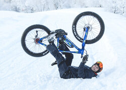 Un eBike rider è sdraiato sulla schiena nella neve e solleva la sua eBike per una foto.