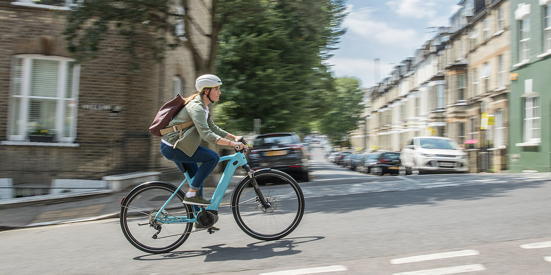 Eine junge Frau fährt auf ihrem hellblauen eBike eine steile Straße in London hinauf