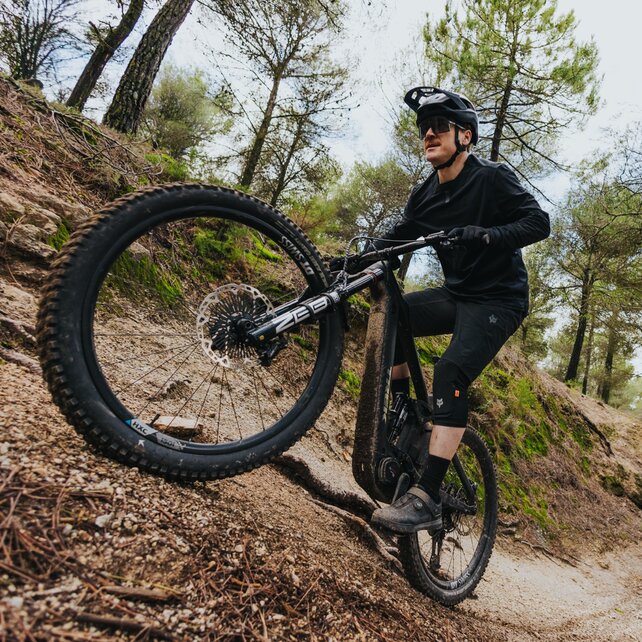 Ein eMountainbiker fährt konzentriert mit seinem schwarzen eBike einen steilen, sandigen Waldweg hinauf.