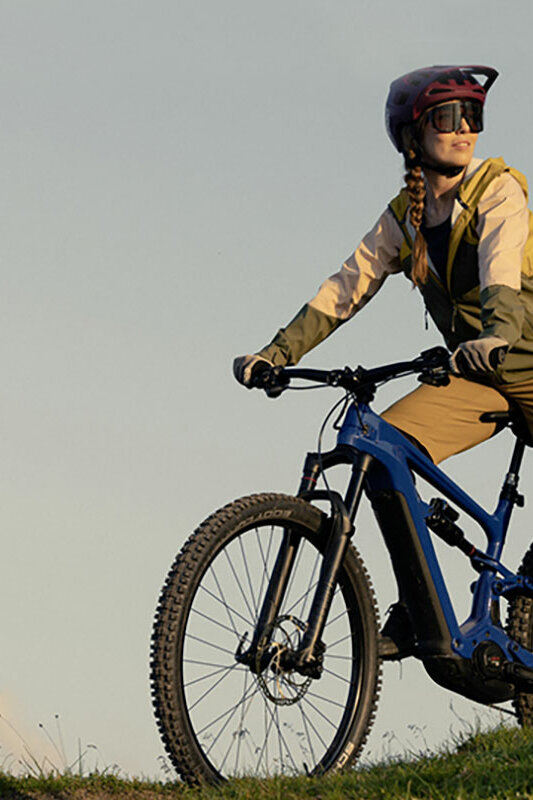 eBike-Fahrerin steht mit ihrem eBike auf einem Hügel und schaut in die Ferne.