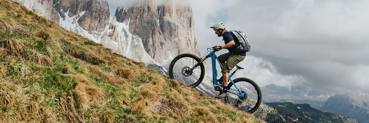 Un homme grimpe une pente raide en VTT électrique, entouré d'un paysage brumeux.