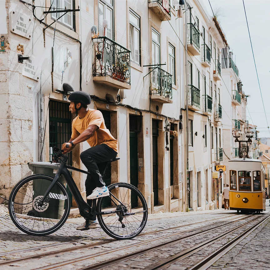 An eBike rider drives over paved ground with tram tracks and turns towards a building.