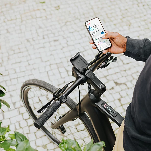 Osoba stojící na elektrokole a držící v ruce smartphone, na kterém je spuštěná aplikace eBike Flow.