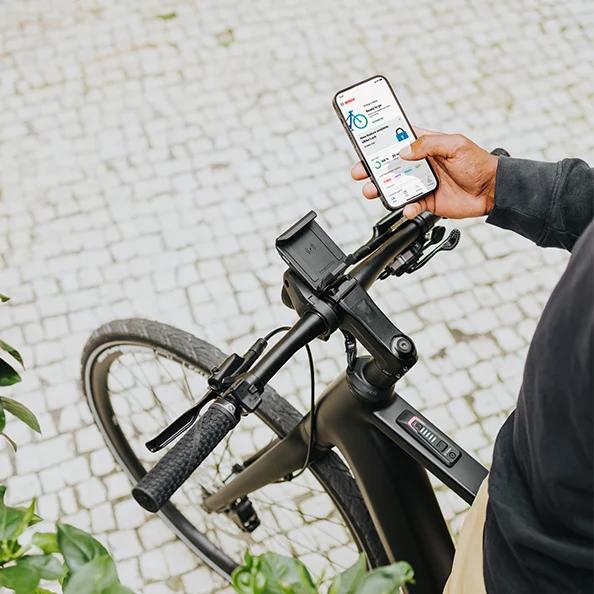 Osoba stojąca na rowerze elektrycznym trzyma w ręku smartfon z otwartą aplikacją eBike Flow.