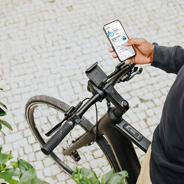 En person står på en eBike och håller en smartphone i handen med eBike Flow-appen öppen.