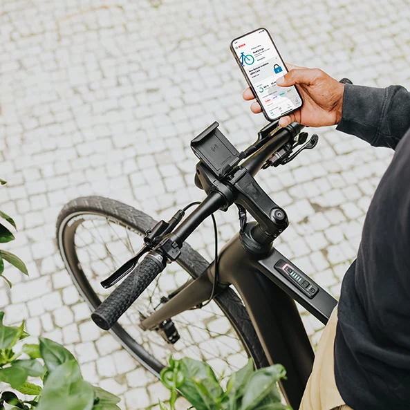 A person is standing on an eBike and holding a smartphone with the eBike Flow app open.