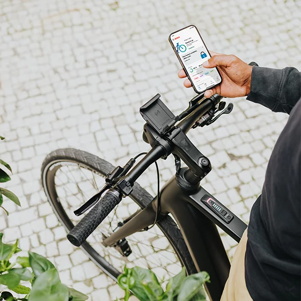 Una persona è in sella a un eBike e tiene in mano uno smartphone con l'app eBike Flow aperta.