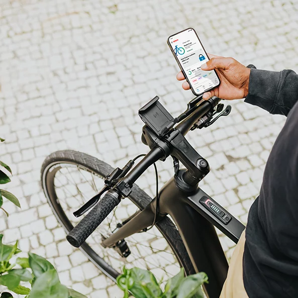 En person står på en eBike og holder en smartphone i hånden med eBike Flow-appen åben.