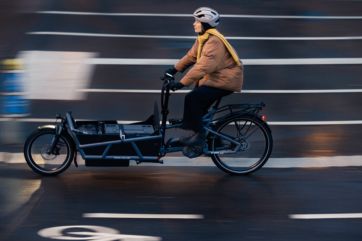Sofie Birc is riding her cargo bike along a bicycle path, with the background blurred.