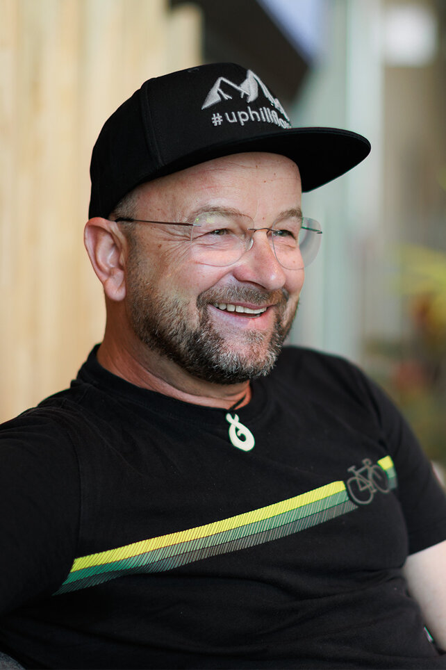 Portrait photo of Stefan Schlie. He is sitting and smiling in front of a blurred background.