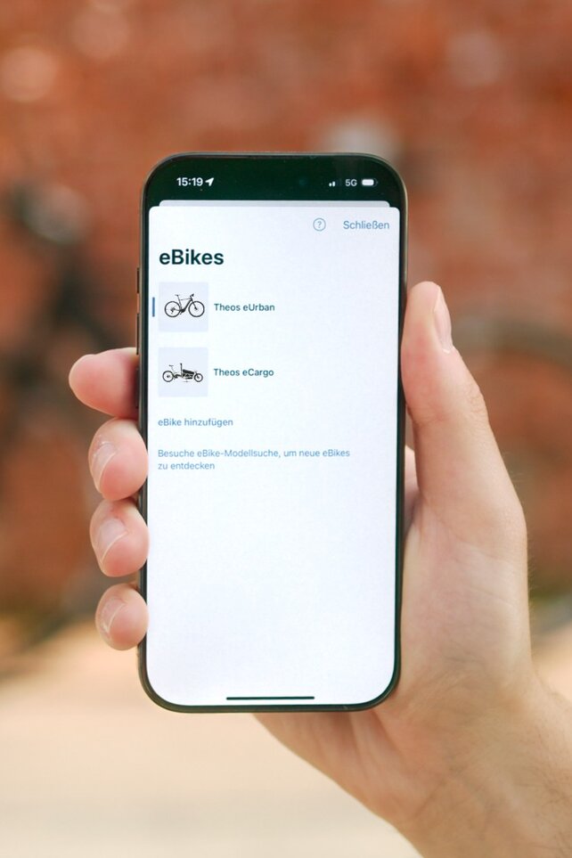Eine Person hält ein Smartphone in der Hand, auf dem eine Liste der eigenen eBikes in der eBike Flow App zu sehen sind.