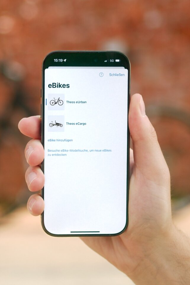 Eine Person hält ein Smartphone in der Hand, auf dem eine Liste der eigenen eBikes in der eBike Flow App zu sehen sind.