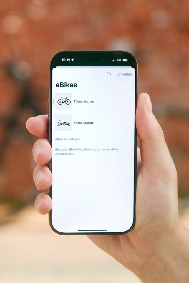 Eine Person hält ein Smartphone in der Hand, auf dem eine Liste der eigenen eBikes in der eBike Flow App zu sehen sind.