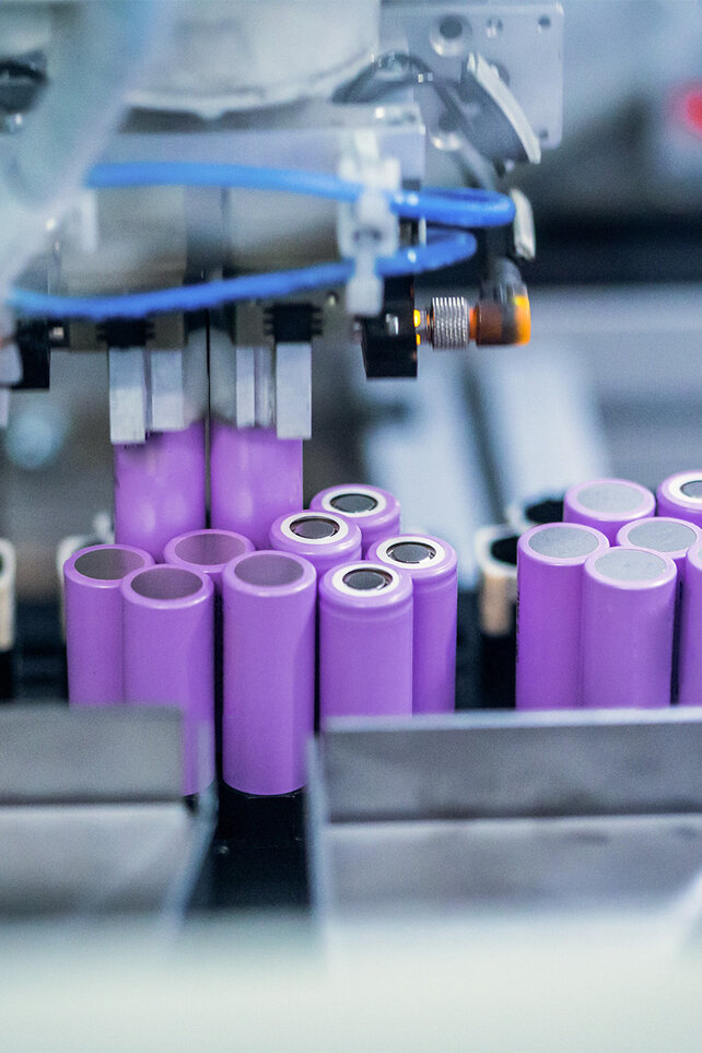 Roboter umhüllt Zellträger mit violettem Kunststoff. Zu sehen sind teils leere, teils mit Zellen gefüllte Kunststoffbehälter.