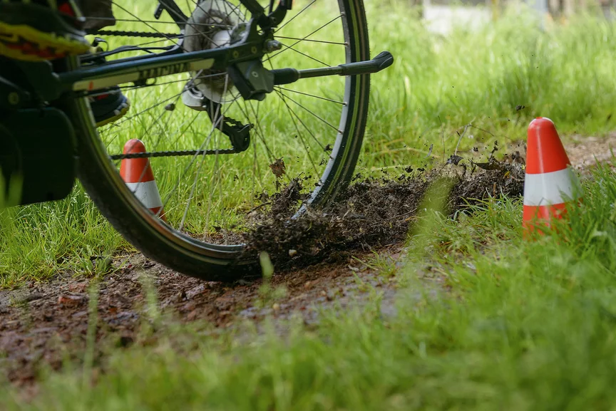 Close-up of a rear wheel driving through two small cones on the earthy ground, surrounded by a meadow.