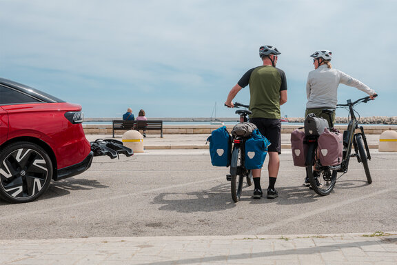 Eine Frau und ein Mann stehen mit ihren vollbeladenen eTrekking-Bikes an einer Straße.