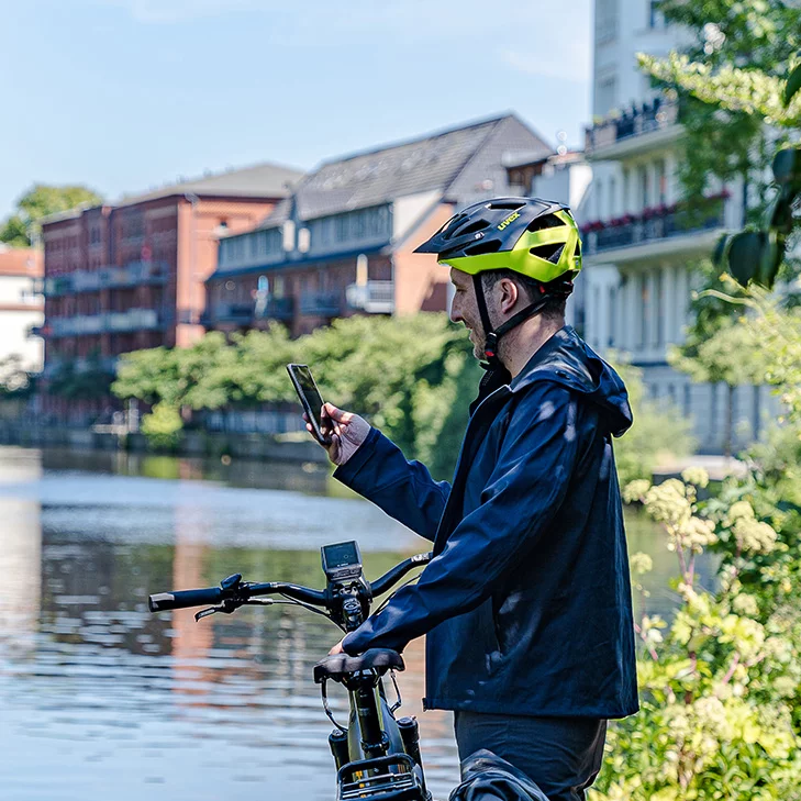 Un homme se tient au bord d'une rivière avec son vélo électrique et regarde son smartphone.