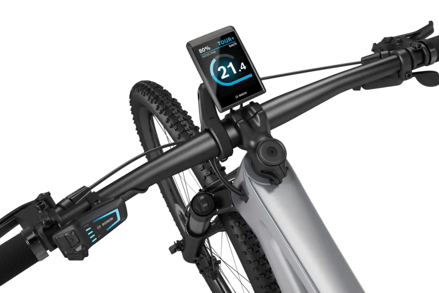 Ein silbernes eMountainbike mit schwarzem Lenker freigestellt vor weißem Hintergrund. Am Lenker ist ein Kiox 500 montiert. Das Display zeigt die Geschwindigkeit in km/h, den Akkustand und den Fahrmodus an.