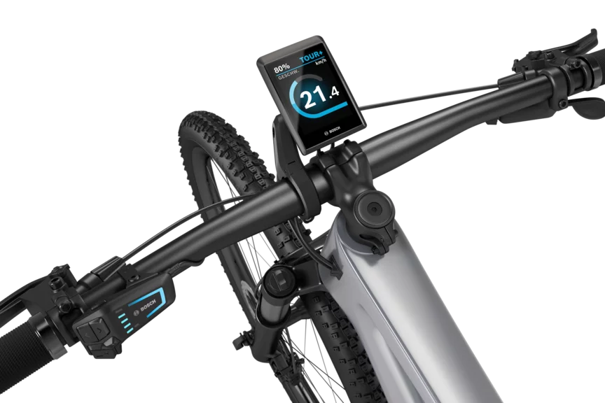 Ein silbernes eMountainbike mit schwarzem Lenker freigestellt vor weißem Hintergrund. Am Lenker ist ein Kiox 500 montiert. Das Display zeigt die Geschwindigkeit in km/h, den Akkustand und den Fahrmodus an.