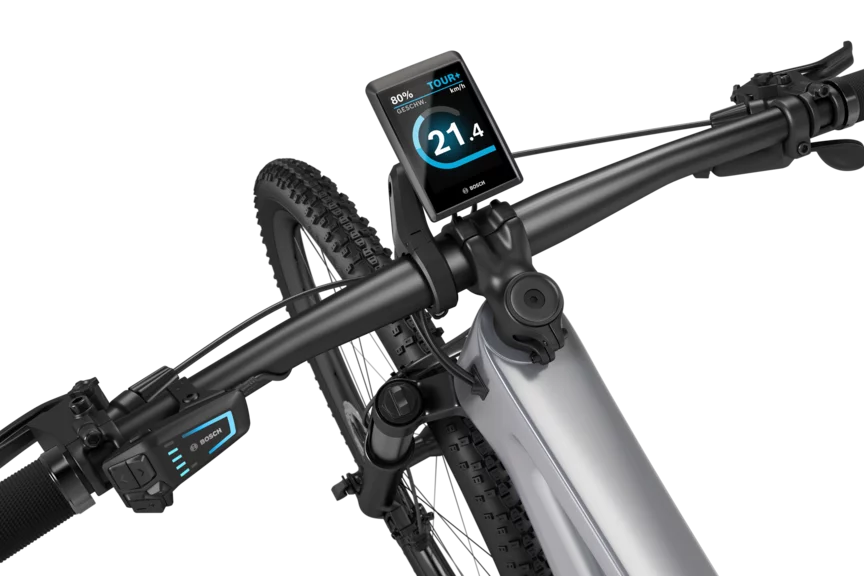 Ein silbernes eMountainbike mit schwarzem Lenker freigestellt vor weißem Hintergrund. Am Lenker ist ein Kiox 500 montiert. Das Display zeigt die Geschwindigkeit in km/h, den Akkustand und den Fahrmodus an.