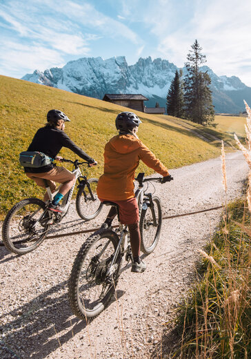 zwei eBiker machen eine Tour im nachhaltigen Urlaub, im Hintergrund sind die Dolomiten in Südtirol zu sehen.