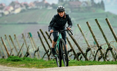 An eBike rider drives up a dirt road, in the background you can see fields and a village.