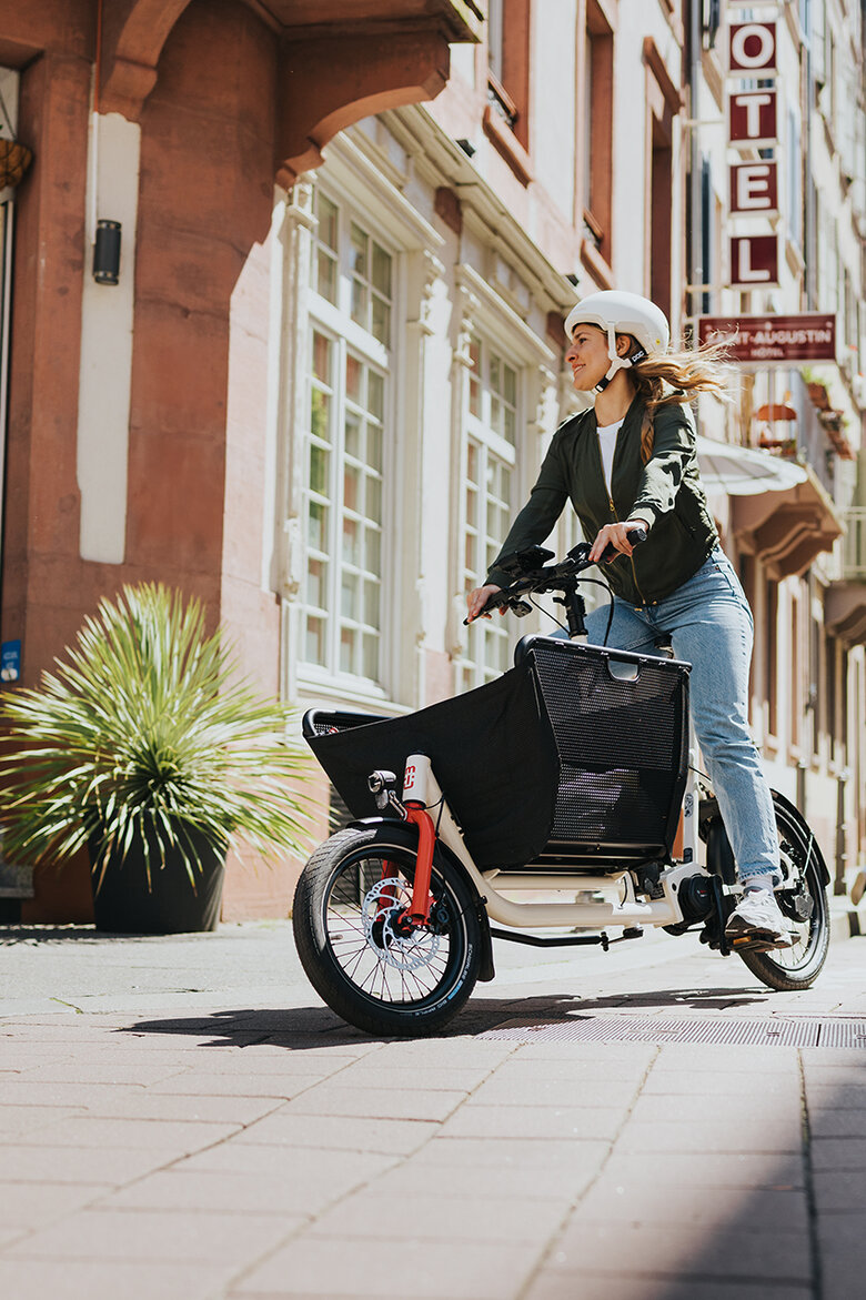 Eine eBikerin mit Fahrradhelm fährt mit einem Bosch eCargo Bike in der Stadt.
