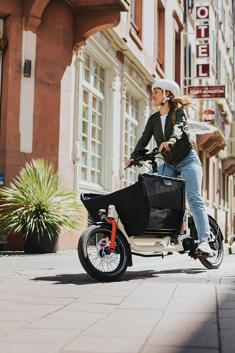 An eBiker with a bicycle helmet rides a Bosch Cargo eBike in the city.