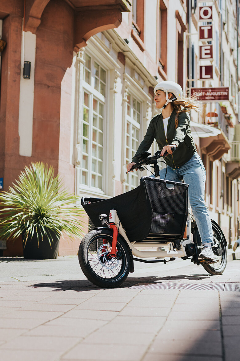 Eine eBikerin mit Fahrradhelm fährt mit einem Bosch eCargo Bike in der Stadt.