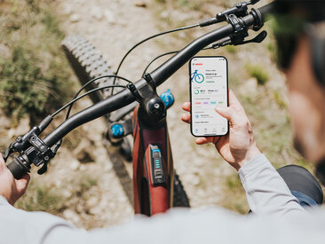 The eBike rider is sitting on his eBike and looking at the home page of the eBike Flow app on his smartphone.