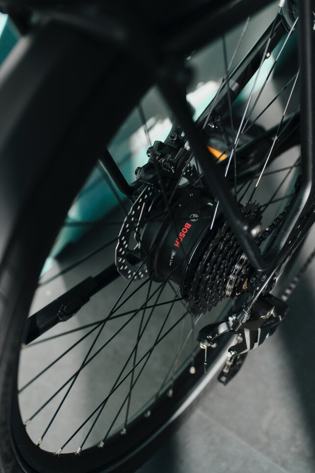 Detalle de la rueda trasera de una eBike. El foco está en la línea del cubo, el motor del buje Bosch. La estética técnica de los componentes de transmisión se destaca gracias a la perspectiva cercana y al juego de luz y sombras.