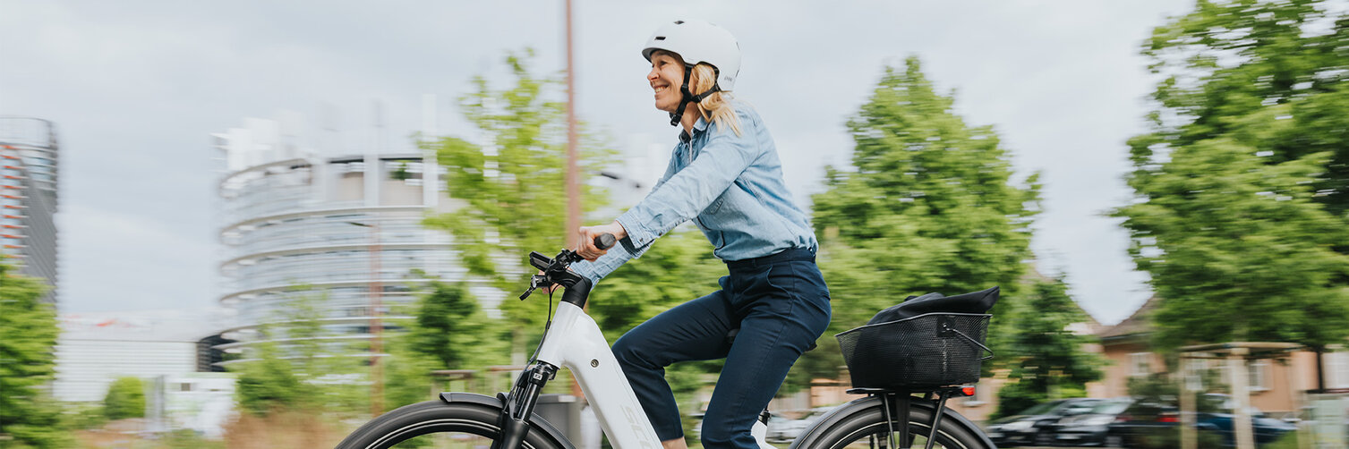 A woman rides her eBike on a street and smiles.
