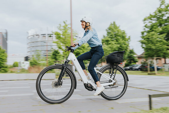 Eine Frau fährt mit ihrem eBike auf einer Straße und lächelt dabei.