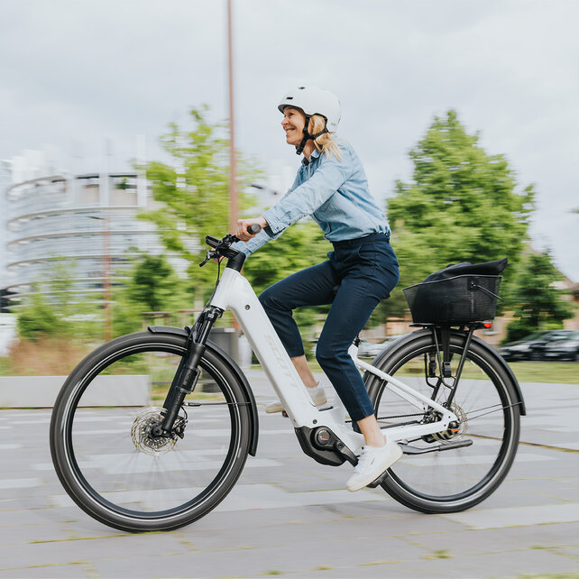 A woman rides her eBike on a street and smiles.